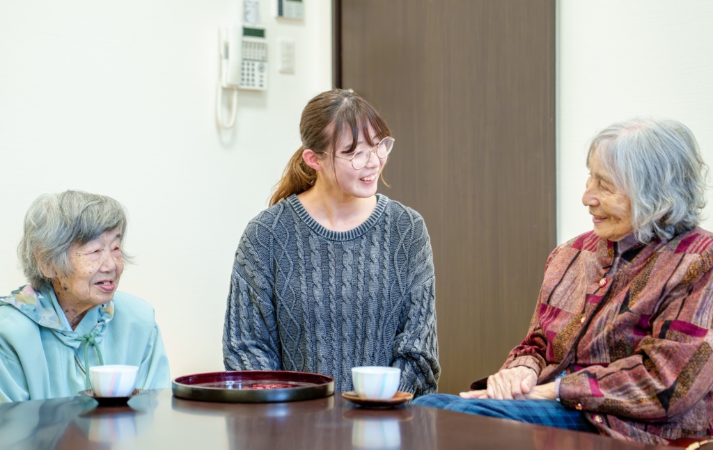 スタッフと入居者がテーブルで談話している様子。コミュニケーションと交流の風景。